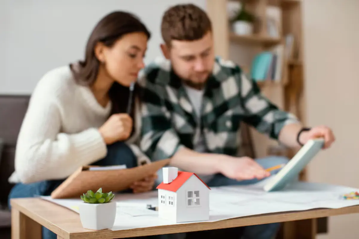 Young couple reviewing documents at home with a miniature house on the table, planning for their First Home Buyer Loan Process in Australia.